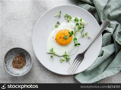 Fried eggs, microgreens and spices on a white plate on concrete background