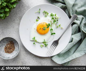 Fried eggs, microgreens and spices on a white plate on concrete background