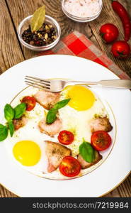 Fried eggs with bacon and vegetables on a white plate. Studio Photo. Fried eggs with bacon and vegetables on a white plate