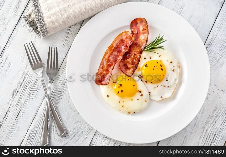 Fried eggs with bacon rashers on the white plate