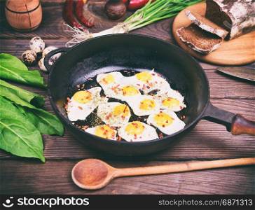 Fried eggs with quail eggs in a black frying pan on a brown wooden background