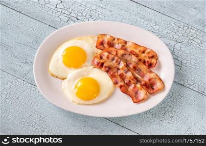 Fried eggs with strips of bacon on the white plate