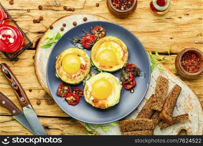 Fried eggs with tomatoes and bread in plate on rustic wooden table. Fried eggs in zucchini
