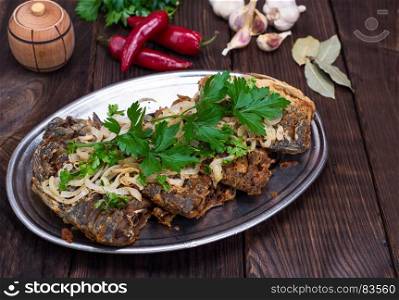 fried fish crucian with onions on an iron plate, top view