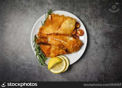 fried fish fillet sliced for steak or salad cooking food with herbs spices rosemary and lemon / tilapia fillet fish crispy served on white plate and dark background