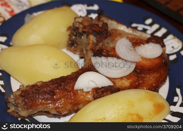 Fried meat on the bone with a fresh onion and boiled potatoes on the plate
