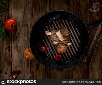 fried meat with bone in the pan on wooden background, top view. dish on a wooden surface