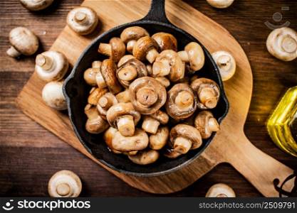 Fried mushrooms in a frying pan on a cutting board. On a wooden background. High quality photo. Fried mushrooms in a frying pan on a cutting board. 