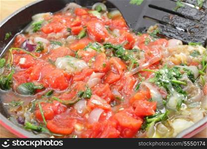 Fried o nion and parsley and tomatoes in a pan, part of the preparation for a greek stuffed aubergine dish, Imam Baildi or Imam melitzanes