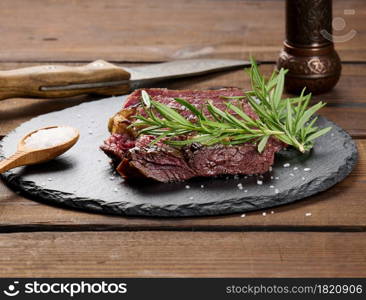 fried piece of beef ribeye cut into pieces on a black board, rare degree of doneness. Delicious steak