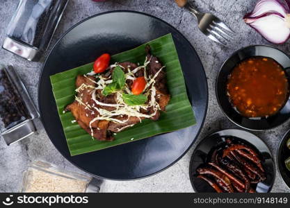 Fried pork topped with sesame seeds along with tomatoes Cabbage and mint, put on a banana leaf in a black dish.