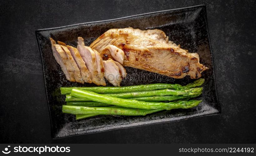fried pork with asparagus and pepper in black ceramic plate on dark tone texture background, top view
