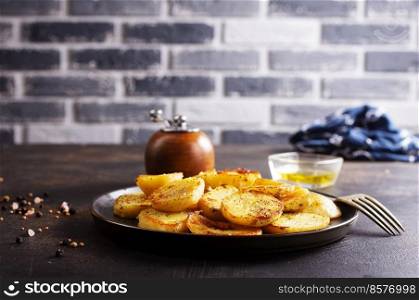 Fried potato wedges with oil, herbs on stone board