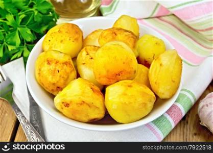 Fried potatoes in a white plate, napkin, parsley, vegetable oil, fork on a wooden boards background