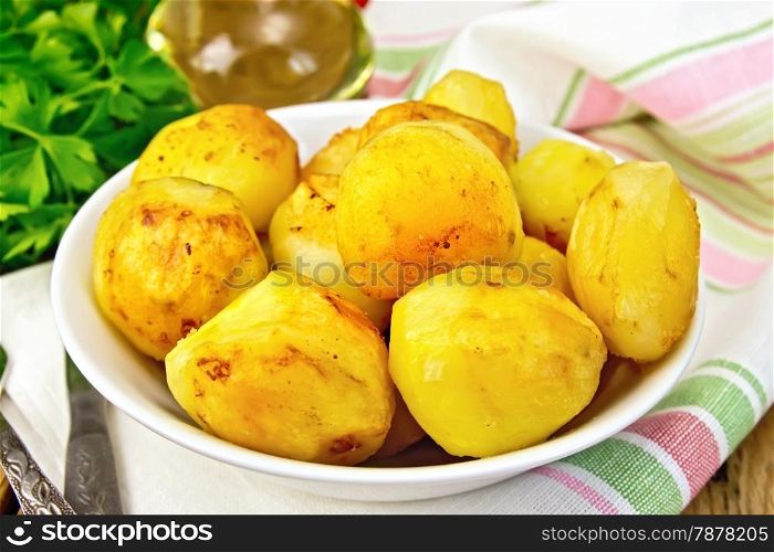 Fried potatoes on a plate on a napkin, parsley, vegetable oil, fork on a wooden boards background