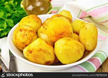 Fried potatoes on a plate on a napkin, parsley, vegetable oil, fork on a wooden boards background