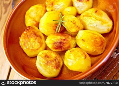 Fried potatoes with rosemary in a ceramic pan on a napkin on a wooden boards background
