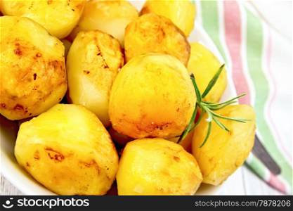Fried potatoes with rosemary in a white plate, napkin, fork on the background light wooden boards