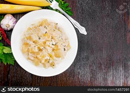 Fried pumpkin with garlic, spices and herbs in a sour cream sauce in a plate, parsley, fork on wooden board background from above