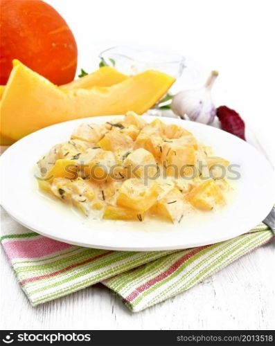 Fried pumpkin with garlic, spices and herbs in sour cream sauce in a plate on kitchen towel, parsley and dill, fork on wooden board background