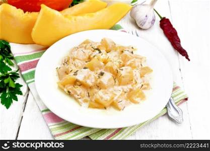 Fried pumpkin with garlic, spices and herbs in sour cream sauce in a plate on napkin, parsley and dill, fork on wooden board background