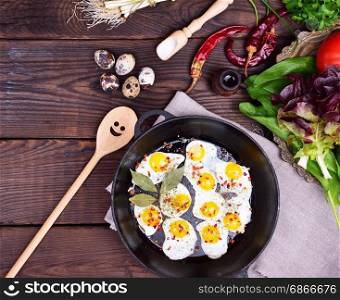Fried quail eggs in a cast-iron frying pan and fresh vegetables, top view