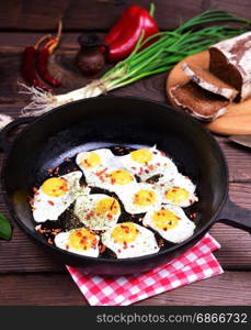 Fried quail eggs with spices in a black cast-iron frying pan, top view