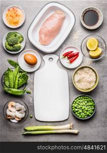 Fried rice cooking ingredients with chicken , egg , shrimps and green vegetables around white cutting board on gray stone background , top view, border. Asian cuisine