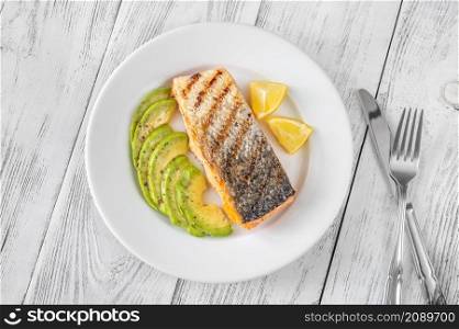 Fried salmon with avocado slices and lemon wedges