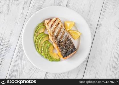 Fried salmon with avocado slices and lemon wedges