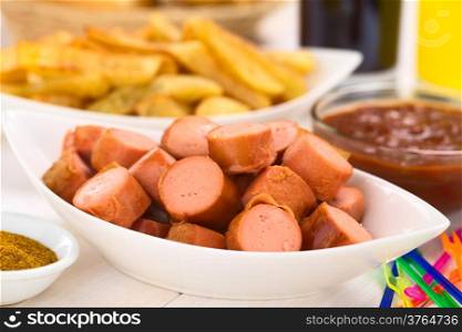 Fried sausage pieces with French fries and curry-ketchup-sauce in the back (Selective Focus, Focus one third into the sausages)