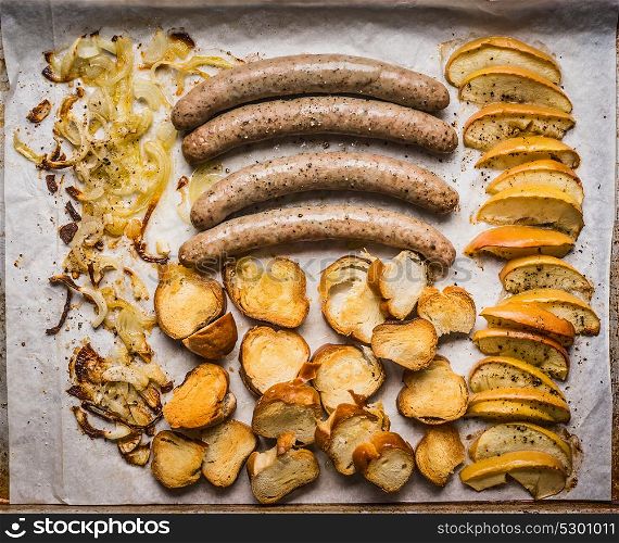 Fried sausages on baking tray with baked apples, onions and lye bun toast , top view, close up. German food