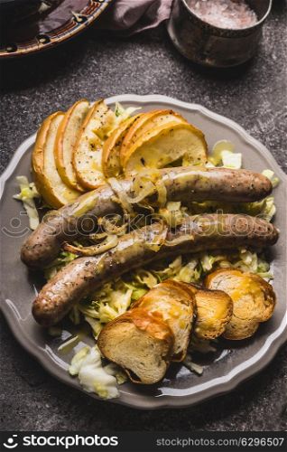 Fried sausages served with baked apples, onions and lye bun toast served on rustic table with white coleslaw salad, top view, close up. German food concept