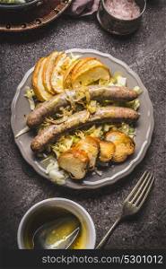 Fried sausages with baked apples, onions and lye bun toast served on rustic table with white coleslaw salad , plates and cutlery top view, place for text. German food concept