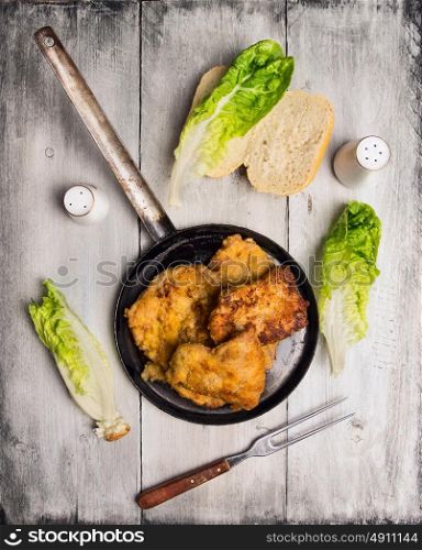 fried schnitzel in old pan on rustic wooden background, top view