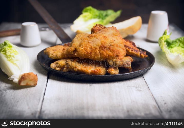 fried schnitzel in pan with green lettuce leaves on old wooden table