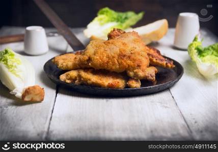 fried schnitzel in pan with green lettuce leaves on old wooden table
