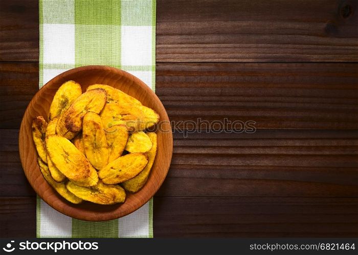 Fried slices of ripe plantains, a traditional and popular snack and accompaniment in Central America and Northern South America, photographed overhead on dark wood with natural light