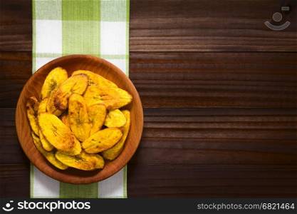 Fried slices of ripe plantains, a traditional and popular snack and accompaniment in Central America and Northern South America, photographed overhead on dark wood with natural light