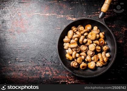 Fried small mushrooms in a frying pan. On a rustic dark background. High quality photo. Fried small mushrooms in a frying pan. 