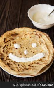 Fried tasty smiling pancakes . Fried smiling pancakes with sour cream on old wooden table