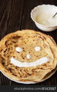 Fried tasty smiling pancakes . Fried smiling pancakes with sour cream on old wooden table
