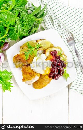 Fried turkey breast in breadcrumbs with cranberry sauce, boiled egg, baked parsnips and lettuce in a plate, towel and fork on wooden board background from above