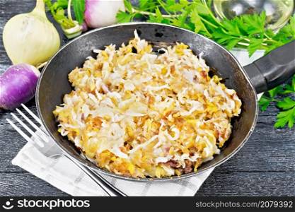 Fried turnips with onions in a frying pan on a towel on dark wooden board background