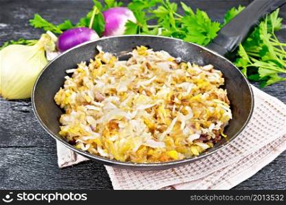 Fried turnips with onions in a frying pan on towel on wooden board background
