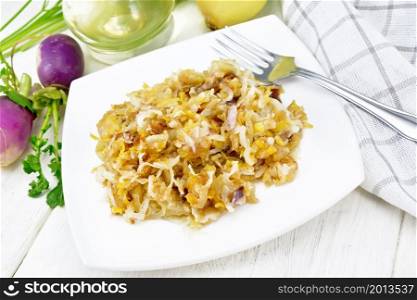 Fried turnips with onions in a plate, oil in decanter, a towel on the background of light wooden board