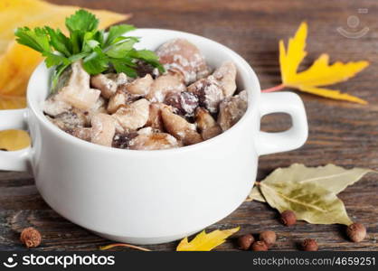 Fried with cream forest mushrooms in white plate and green parsley on a brown wooden background.