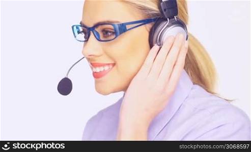 Friendly call centre operator wearing glasses and a headset giving a beautiful smile as she listens to the clients call