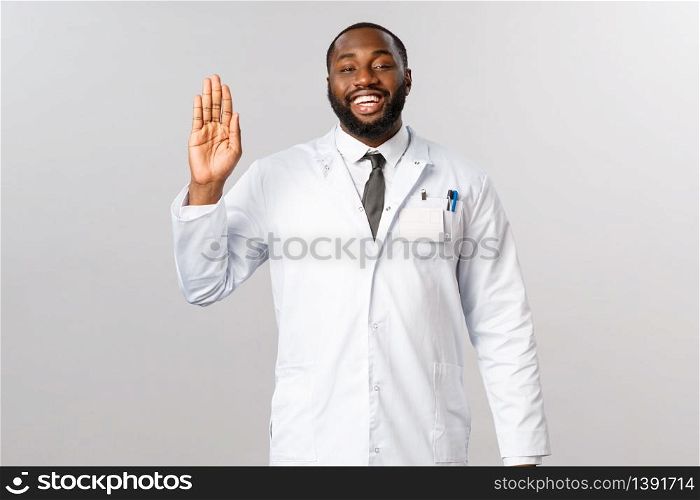 Friendly cheerful african-american doctor inviting patients for check-up, greeting people with optimistic joyful smile, waving hand, saying buy never come back to hospital, stay healthy.. Friendly cheerful african-american doctor inviting patients for check-up, greeting people with optimistic joyful smile, waving hand, saying buy never come back to hospital, stay healthy