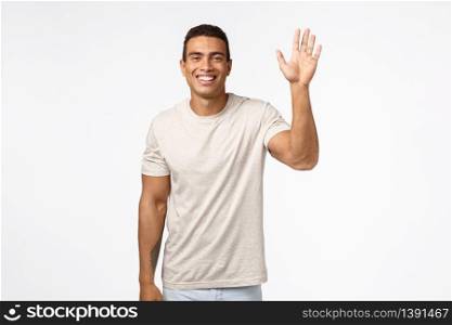Friendly cheerful athletic man in t-shirt, raising one hand and waving in hello, hi, greeting gesture, smiling delighted and upbeat, see friend meeting someone, standing white background joyful.. Friendly cheerful athletic man in t-shirt, raising one hand and waving in hello, hi, greeting gesture, smiling delighted and upbeat, see friend meeting someone, standing white background joyful